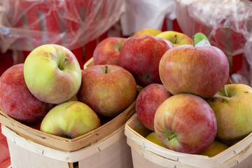A stack or bulk supply of large red ripe Fuji apples on a table for sale at a farmer's market. The apples are stacked in wooden baskets for sale. The red organic apples are fresh sweet produce.