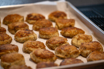 A tray of cooked round salt cod fishcakes prepared on a barbeque. The savory, potato, salt codfish, and butter mixture are shaped into small patties and fried in butter until golden brown.