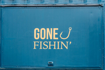A blue metal wall with a window with gone fishing painted in yellow text and a fishing hook symbol....