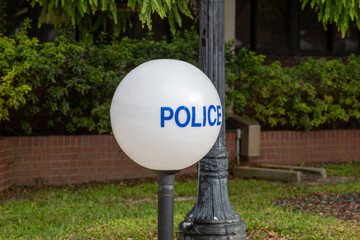 An illuminated round white globe made of glass with blue lettering. The police sign is on a black...