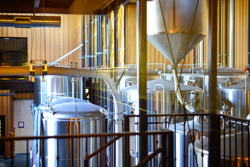 The interior production room of a microbrewery. Multiple large stainless steel brewing vats with...
