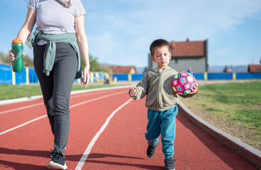 Toddler with soccer ball running on track with his aunt