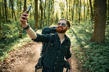 Phone in hand. Bearded man is in the forest at daytime