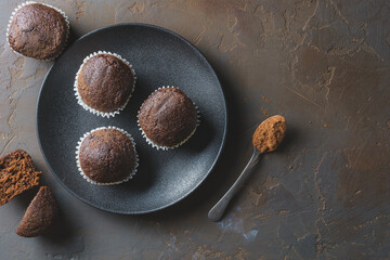 Delicious chocolate muffins on a black plate and on a concrete table. Top view with space for text.