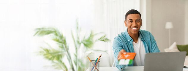 An african american man smiling and presenting a gift card in a home setting with ample copy space and suitable for a web-banner