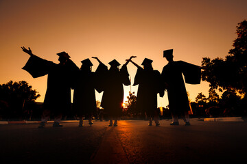 silhouette cheerful graduates group in black gowns Graduation at sunset