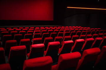 Rows of empty red seats in a dark cinema hall, illuminated by a red glow from the screen, creating...