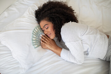 Hispanic woman is seen lounging on a bed with a fan of money spread out in front of her. She...