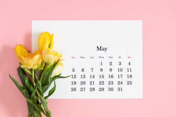Flat lay of paper desk calendar for May 2024, top view. A bouquet of bright colorful tulips on pastel pink background