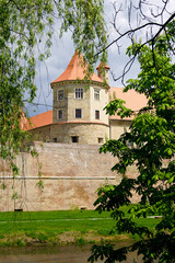 Landscape from the Romanian city of Fageras: a fortress tower, an ancient defensive wall and trees growing on the banks of a moat with water.