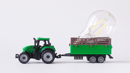 Modern energy-saving transparent LED lamp in the trailer of a green toy tractor. Concept of transportation and delivery services for fragile goods. White background. Photo.