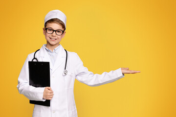 Professional recommendation. Cute little boy in doctor uniform pointing at empty space on orange...