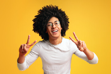 Cool african american guy smiling and demonstrating v-signs, orange studio background, panorama