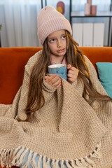 Sick ill girl child wrapped in blanket shivering from cold drinking hot herbal medical tea in...