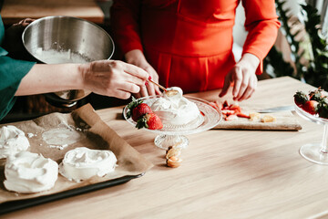 A chef in a teal apron carefully shapes meringues on a baking sheet, surrounded by a lively kitchen...