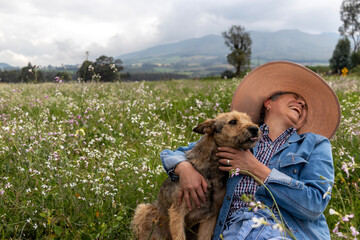 A mature woman laughing while her dog sticks out its tongue. The woman is dressed for a day in the countryside. Color image with negative space