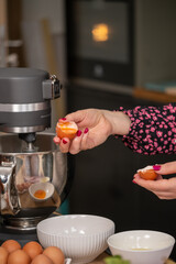 Precise egg separation performed by a chef in a floral blouse, a critical step in preparing ingredients for a sophisticated recipe in a well equipped kitchen.
