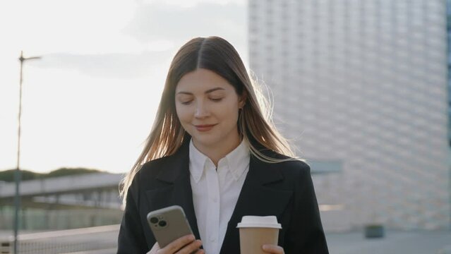 Young businesswoman in a black suit looking at her phone in front of office buildings 