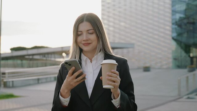 Young businesswoman in a black suit looking at her phone in front of office buildings 