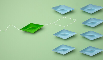 Group of blue paper boats heading in one direction and one green one heading in the opposite direction.
