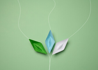 Paper boats on a green background with paths of movement, representing the concept of individuality.