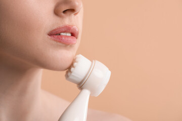 Washing face. Young woman with cleansing brush on beige background, closeup. Space for text