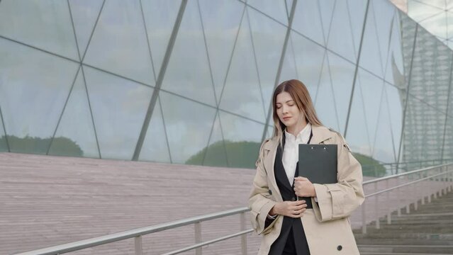 Young businesswoman in a white shirt and coat walking in front of office buildings