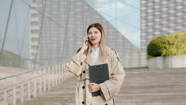 Young businesswoman in a black suit talking on the phone while holding a folder