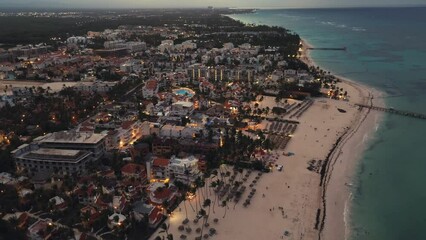 Mesmerizing drone captures coastal city at dusk, offering breathtaking aerial perspective. Sparkling city lights below create stunning scene in this tourist hotspot situated in Punta Cana, Dominican