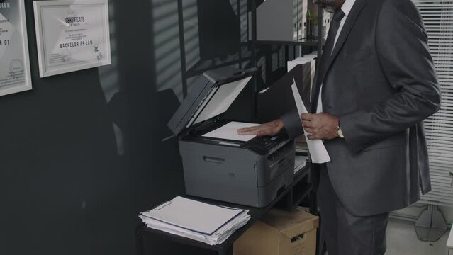 Side tilt footage of male lawyer in suit making copy or scan of legal documents using multi-function printer in modern office
