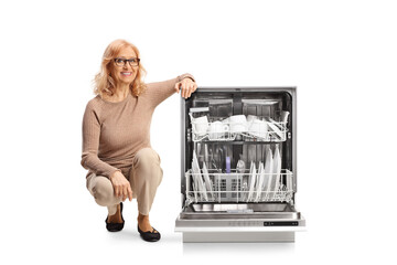 Middle aged woman kneeling next to a dishwasher
