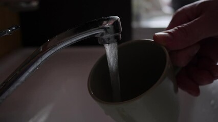 Water pours from tap into mug. Close up.