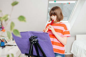 A teenage girl plays a musical instrument, the flute, in her room at home. Music lessons at home....