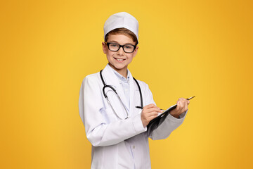 A smiling child in a medical coat holds a clipboard and poses like a healthcare professional.