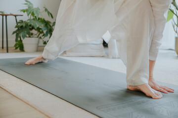 an asian woman wearing loosing white clothes doing yoga at home