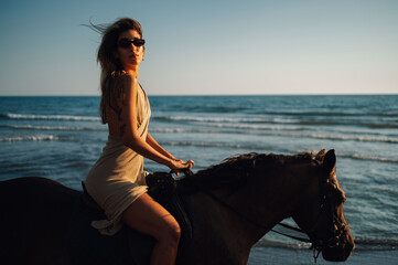 Side view of a beautiful woman horseback riding on a beach during a sunset