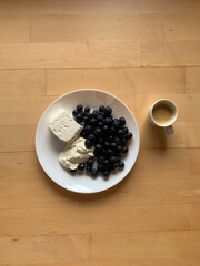 A cup of espresso coffee and a plate with cottage cheese, sour cream and blueberries stand on a wooden background. View from above. Place for text.