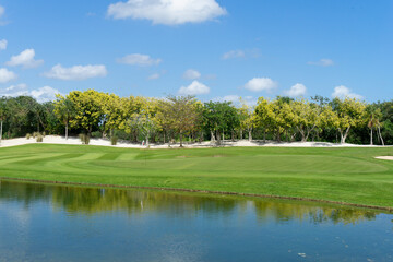 Overview of a golf course with reflecting pond, vibrant greens, fairways and tropical trees on a sunny day in Mexico. Ideal for backgrounds with copy space in the blue sky