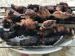 Overcooked meat on metal skewers after coals in the grill lies on a white plate on the table....
