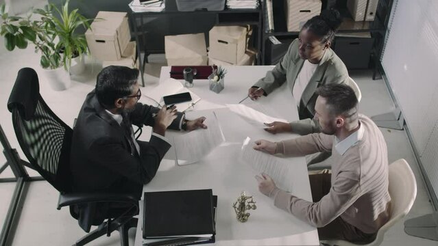 Overhead footage of senior barrister consulting diverse female and male customers and helping them make up bargain and sale agreement during workday in modern office