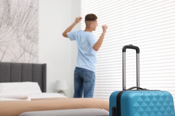 Guest stretching in stylish hotel room, focus on suitcase