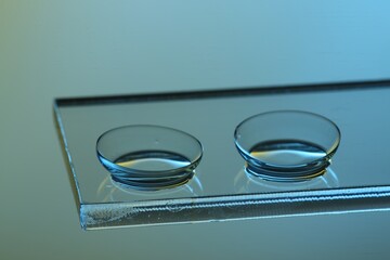 Pair of contact lenses on glass against light blue background, closeup