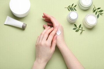 Woman applying hand cream on green background, top view