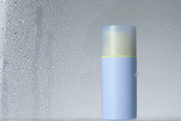 Bottle with moisturizing cream on light background, view through wet glass. Space for text