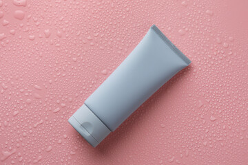 Moisturizing cream in tube on pink background with water drops, top view