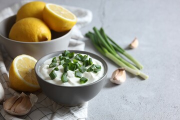 Delicious yogurt with green onion, garlic and lemons on light textured table, closeup