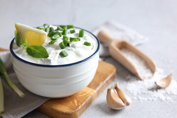 Delicious yogurt with green onion in bowl, garlic, salt and lemon on light textured table, closeup