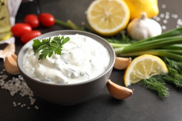Delicious yogurt in bowl and ingredients on black table, closeup