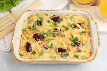 Tasty sausage casserole with green onions in baking dish on white table, closeup