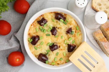 Tasty sausage casserole with green onions in baking dish served on white tiled table, flat lay